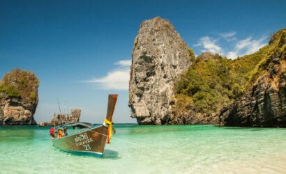 Home A picturesque tropical beach with a traditional boat and stunning limestone cliffs in clear turquoise waters.